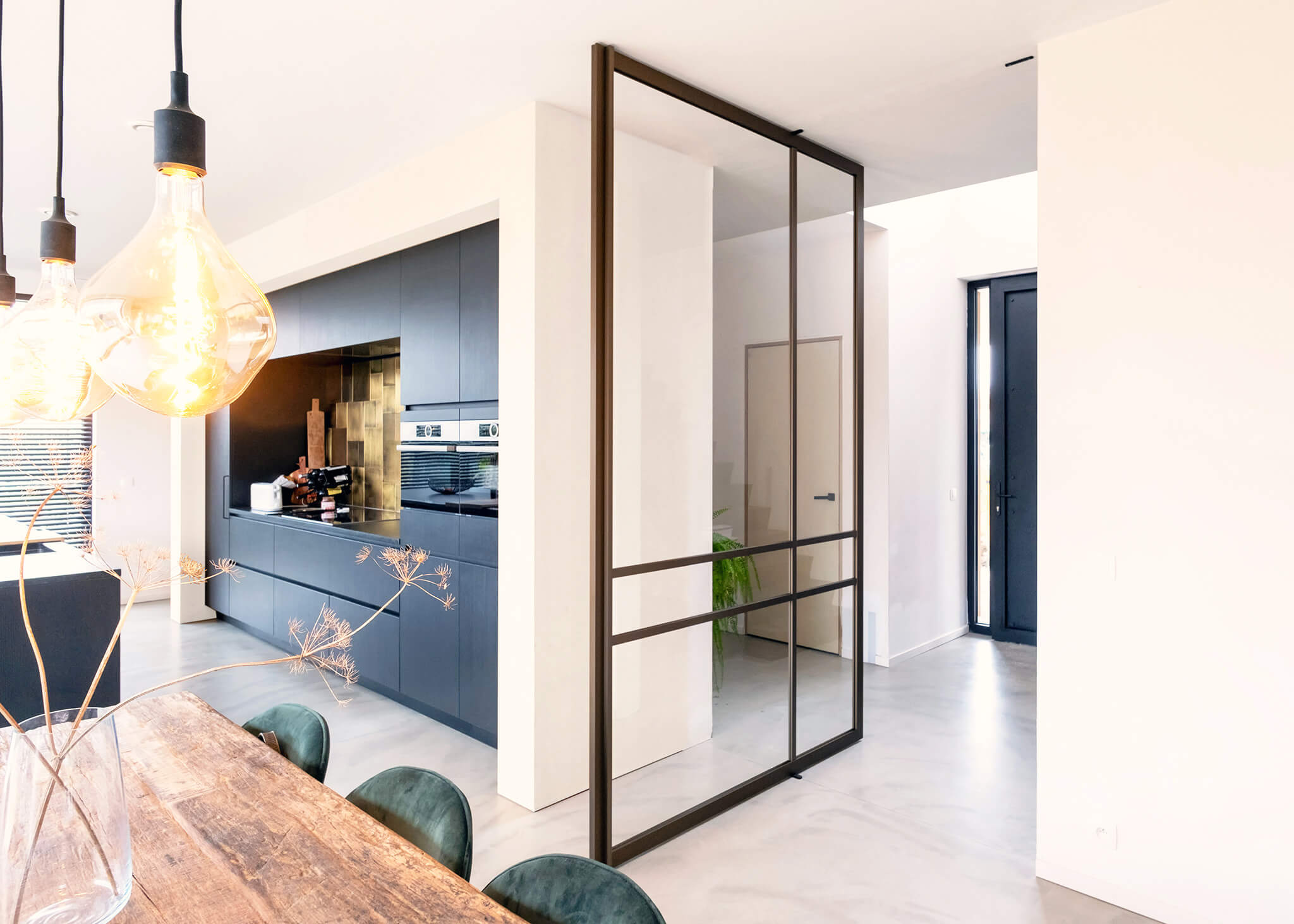 ANYWAYdoors steel look door, a large modern glass door with horizontal and vertical lines in steel look optics. The door is open and leading into a kitchen and dining room. the overall kitchen is modern, has light beige walls and a wooden table